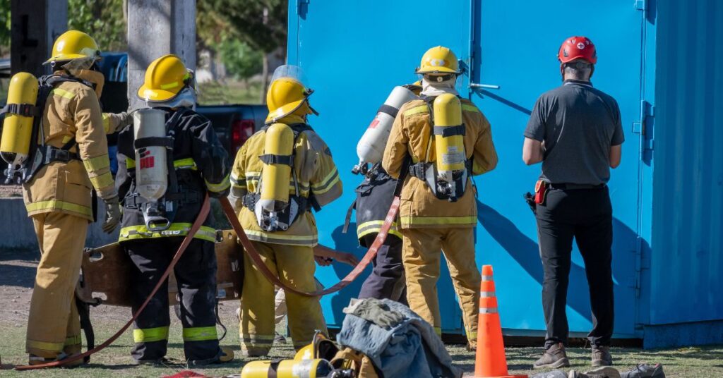 Firefighters in protective gear gather around a blue door, ready for action in a firefighting scenario.