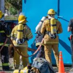 Firefighters in protective gear gather around a blue door, ready for action in a firefighting scenario.